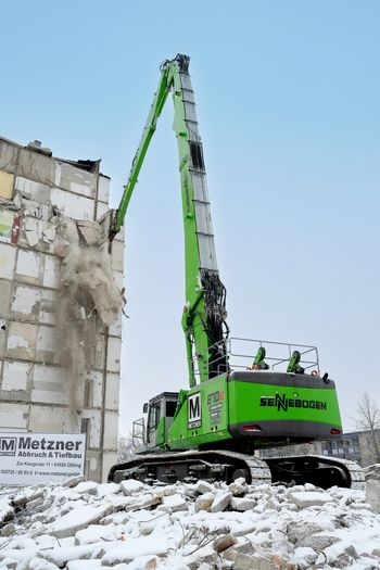 SENNEBOGEN 870 E demolition excavator using demolition shears to dismantle the top floor of a high-rise building.