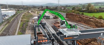 A SENNEBOGEN 840 E rail-mounted material-handling excavator loading roundwood at a timber-handling facility.