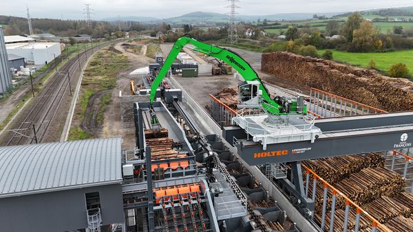 A SENNEBOGEN 840 E with a grapple, precisely feeding round timber into the HOLTEC feed unit.