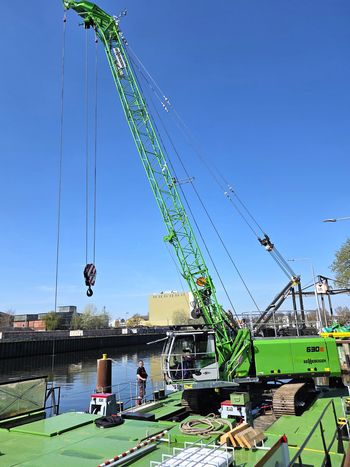 A SENNEBOGEN 630 E cable excavator mounted on a pontoon, being used as a floating grab on a waterway.