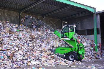 SENNEBOGEN 360 G telehandler transporting recyclable material with a bucket at a recycling facility.