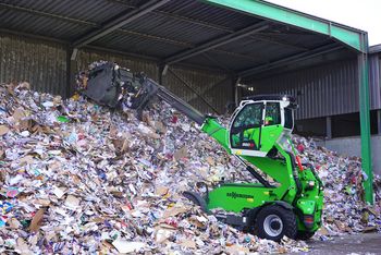 SENNEBOGEN 360 G Teleskoplader transportiert Recyclingmaterial mit einer Schaufel auf einem Recyclinghof.