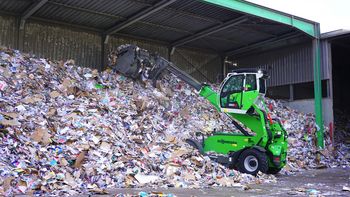 SENNEBOGEN 360 G telehandler transporting recyclable material with a bucket at a recycling facility.