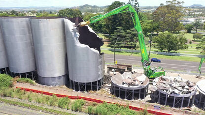 SENNEBOGEN 870 E demolition excavator demolishing silos between main road and railway tracks