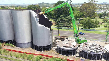 SENNEBOGEN 870 E demolition excavator demolishing silos between main road and railway tracks