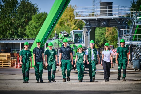 Neue Auszubildende von SENNEBOGEN in Arbeitskleidung und Schutzhelmen an ihrem ersten Arbeitstag auf dem Werksgelände.