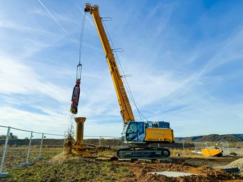 SENNEBOGEN 624 E Seilbagger hebt ein gelbes Anbaugerät mit seinem Seilgehänge auf dem Betriebsgelände.