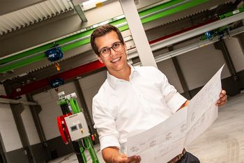Sebastian Sennebogen mit Bauplan vor einer SENNEBOGEN Maschine.