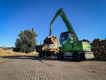 SENNEBOGEN 730 E pick-and-carry machine handling logs at a trailer in a sawmill.