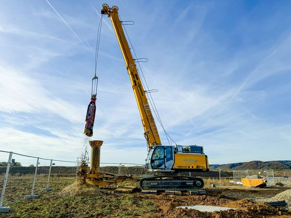 SENNEBOGEN 624 E Seilbagger hebt ein gelbes Anbaugerät mit seinem Seilgehänge auf dem Betriebsgelände.